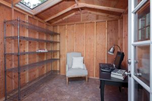The interior of a shed with an office desk, chair, and metal shelving.
